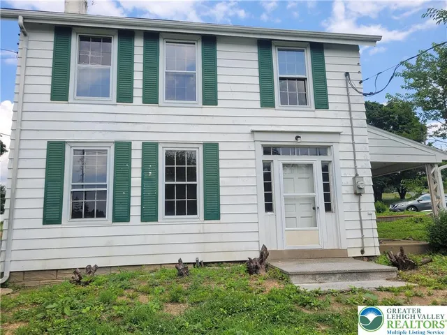 a view of a house with small yard plants and a large tree
