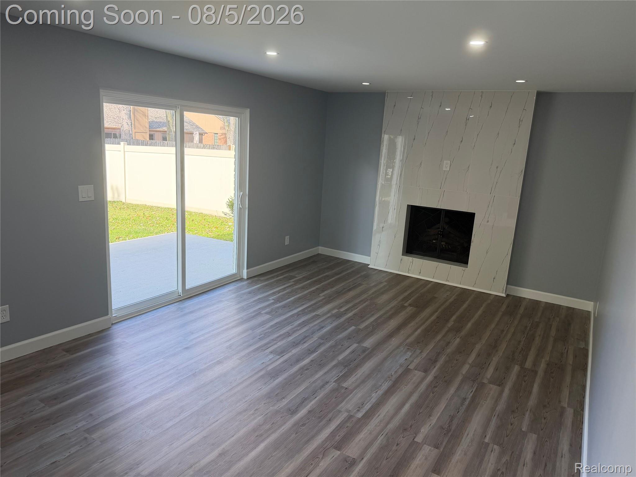 20698 Coachwood Road Riverview, MI 48193 - Photo 9 of 37 Spacious living area featuring a modern fireplace with a white, patterned surround, wood-finish flooring, recessed lighting, and a sliding glass door leading to an outdoor patio and fenced yard