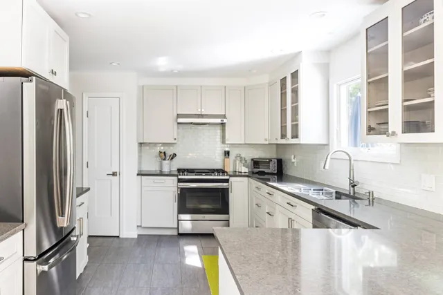 a kitchen with stainless steel appliances granite countertop a refrigerator a sink a stove and white cabinets with wooden floor