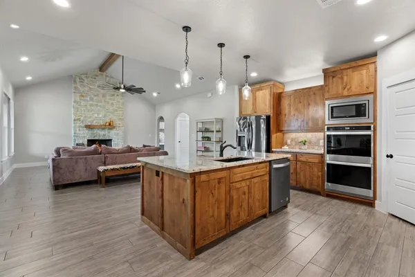 a kitchen with stainless steel appliances a stove a sink dishwasher a refrigerator and white cabinets with wooden floor