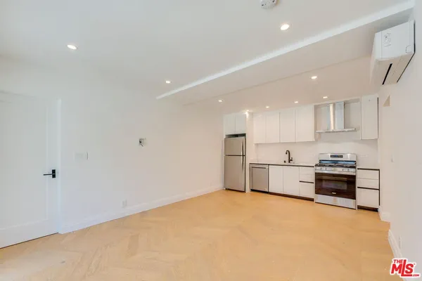 a large white kitchen with a stove a sink a refrigerator and white cabinets with wooden floor