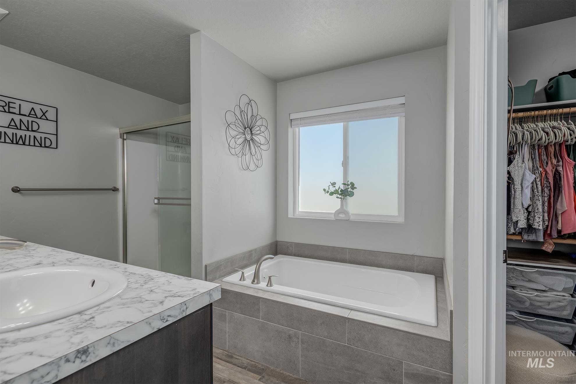 1049 Price Road Weiser, ID 83672 - Photo 14 of 47 Bathroom featuring a built-in soaking tub with tile surround, a single vanity with a white countertop and integrated sink, a glass-enclosed shower, and a dedicated closet space with built-in shelving and hanging rods