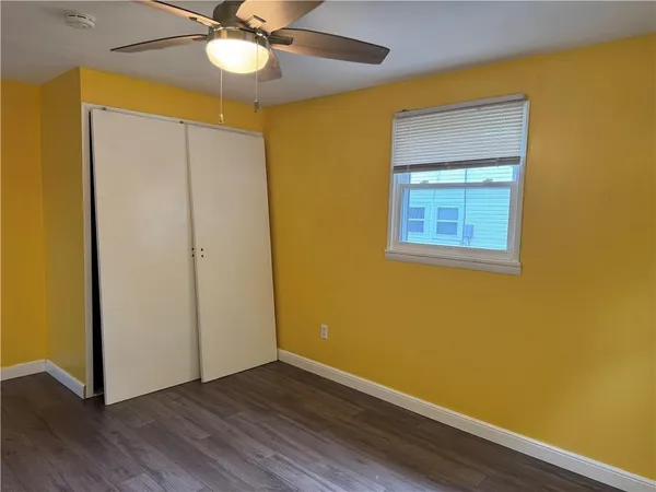 a view of an empty room with wooden floor and a ceiling fan