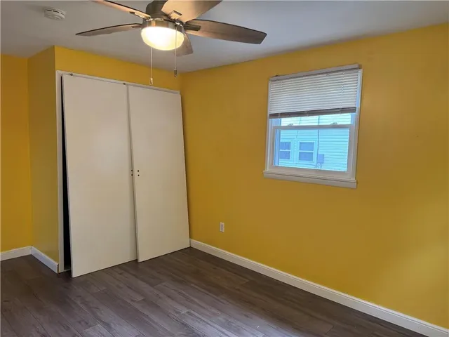 a view of an empty room with wooden floor and a ceiling fan