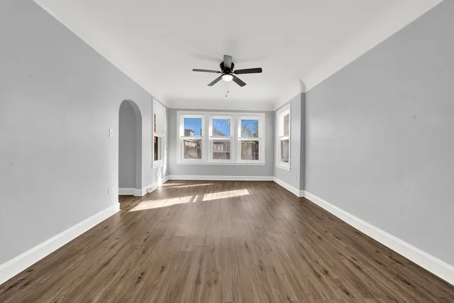 an empty room with wooden floor ceiling fan and windows