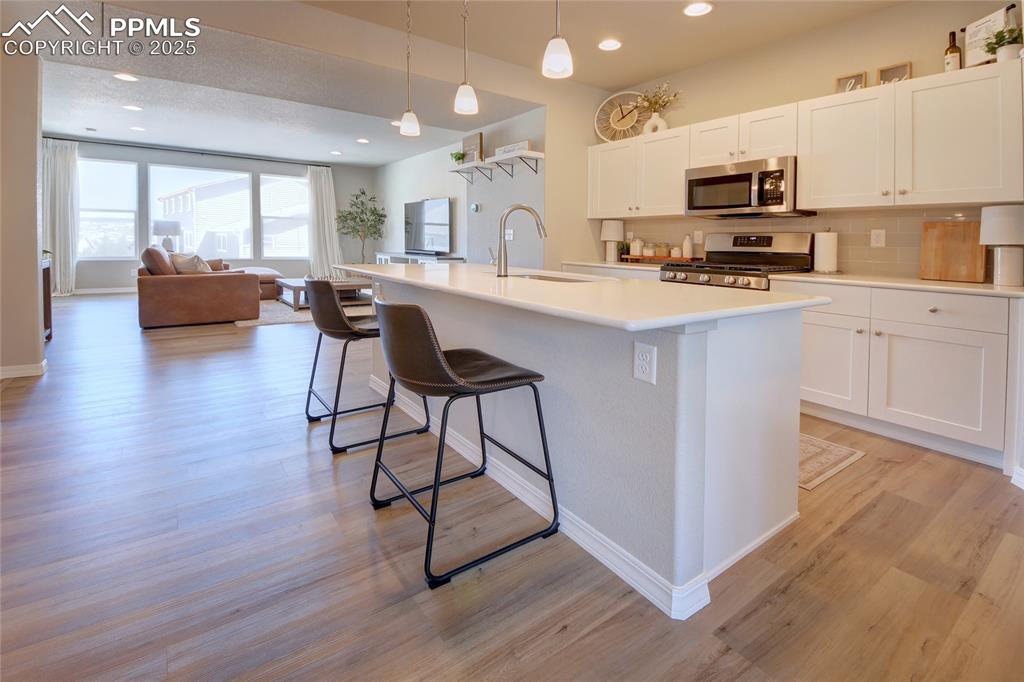 6069 Inman View Colorado Springs, CO 80924 - Photo 8 of 38 a kitchen with stainless steel appliances a microwave a stove a sink dishwasher a microwave oven and a dining table with wooden floor