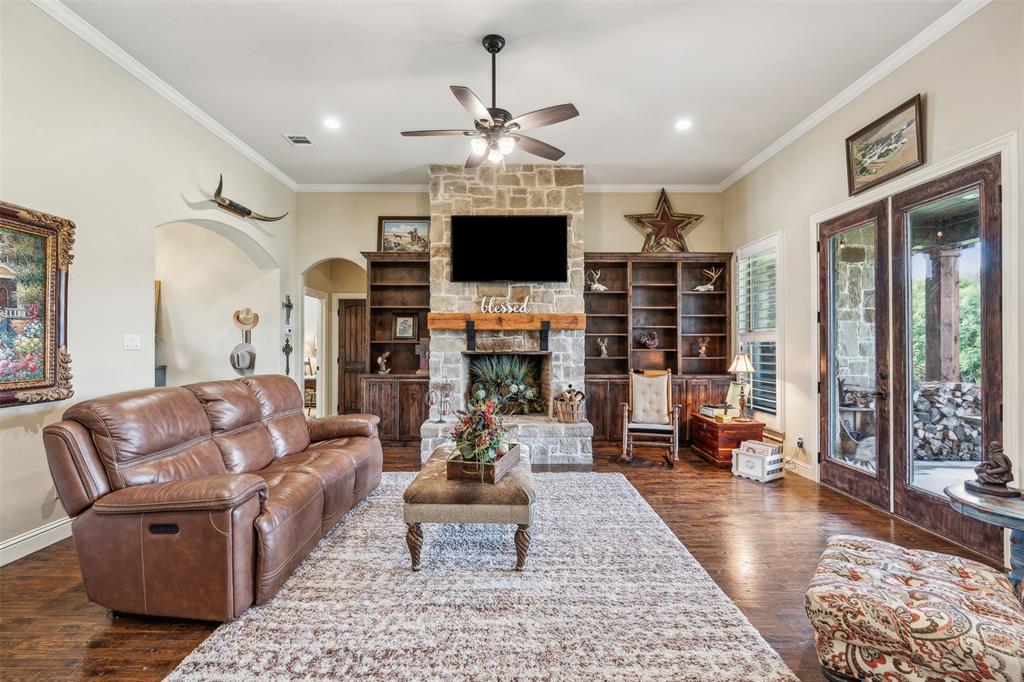 4180 North Smith Road Fate, TX 75087 - Photo 6 of 27 Living room featuring a stone fireplace, dark wood-type flooring, ceiling fan, and ornamental molding