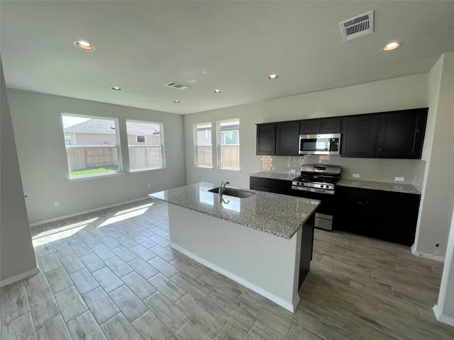 a large kitchen with granite countertop a stove a sink a refrigerator counter space and wooden floor