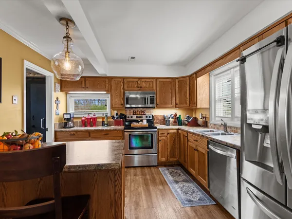 a kitchen with stainless steel appliances granite countertop a refrigerator a sink dishwasher a stove and white countertops with wooden floor