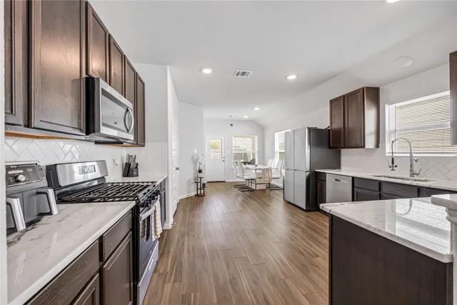 a kitchen with stainless steel appliances granite countertop a sink stove microwave refrigerator and wooden cabinets