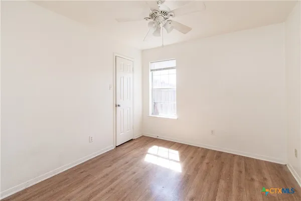 an empty room with wooden floor chandelier fan and windows