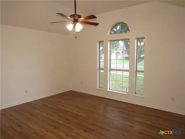 an empty room with wooden floor fan and windows