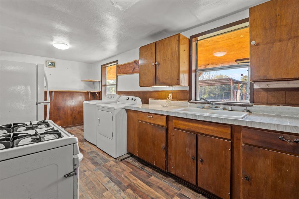 205 College Street Chico, TX 76431 - Photo 12 of 40 Kitchen with white appliances, light countertops, dark wood-style flooring, brown cabinetry, and washing machine and dryer
