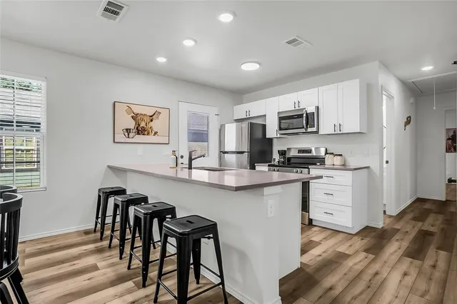 a kitchen with stainless steel appliances granite countertop a stove top oven a sink a dining table and chairs with wooden floor