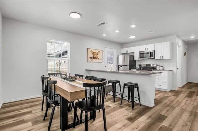 a kitchen with stainless steel appliances kitchen island granite countertop a dining table chairs and a refrigerator