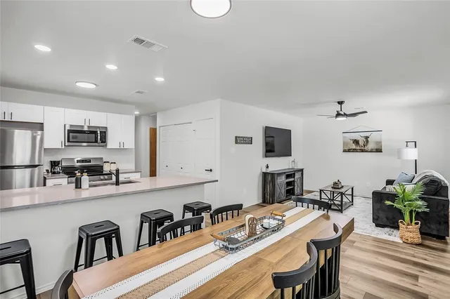 a kitchen with stainless steel appliances granite countertop a stove top oven a sink a dining table and chairs with wooden floor