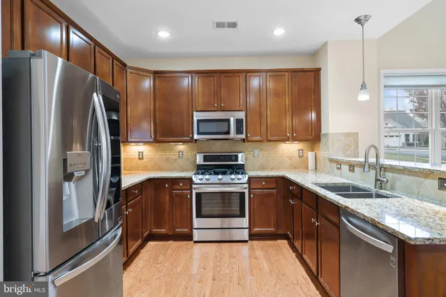 a kitchen with stainless steel appliances granite countertop a stove a sink and a refrigerator with wooden floor