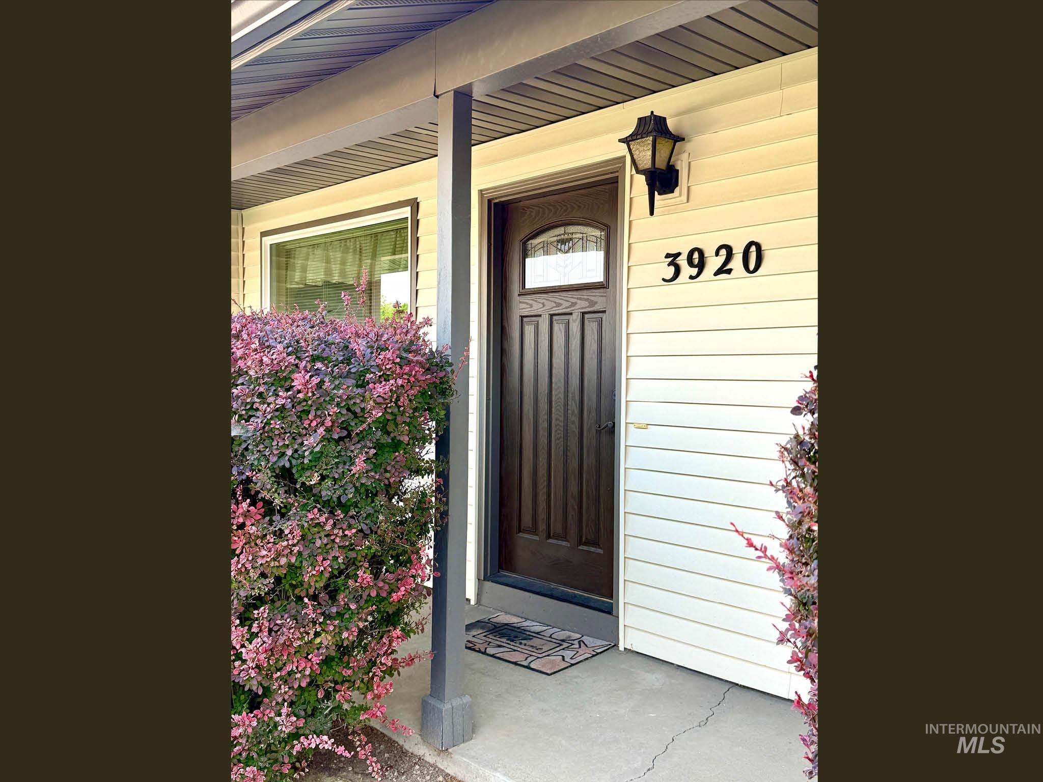 Wood-panel front door with arched glass insert, flanked by a black wall-mounted lantern light fixture