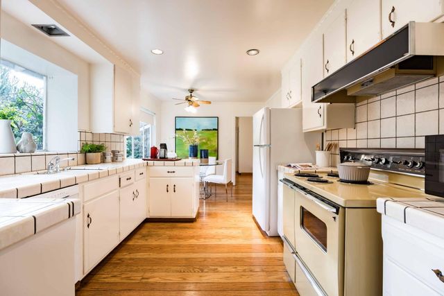 a large kitchen with stainless steel appliances granite countertop a stove a sink dishwasher and white cabinets with wooden floor