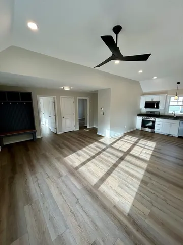 a view of an empty room and kitchen with wooden floor