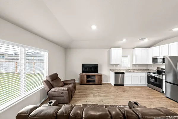 a living room with stainless steel appliances furniture a flat screen tv and windows