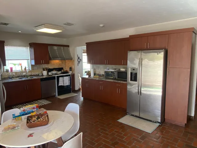 a kitchen with stainless steel appliances granite countertop a refrigerator a stove a sink a dining table and chairs