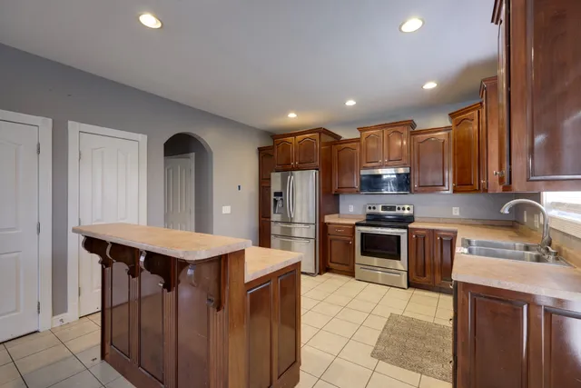 a kitchen with stainless steel appliances granite countertop a sink a stove a refrigerator and a oven with wooden cabinets