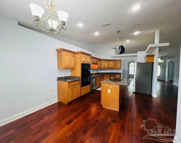 a kitchen with stainless steel appliances granite countertop a refrigerator a stove top oven and wooden floor