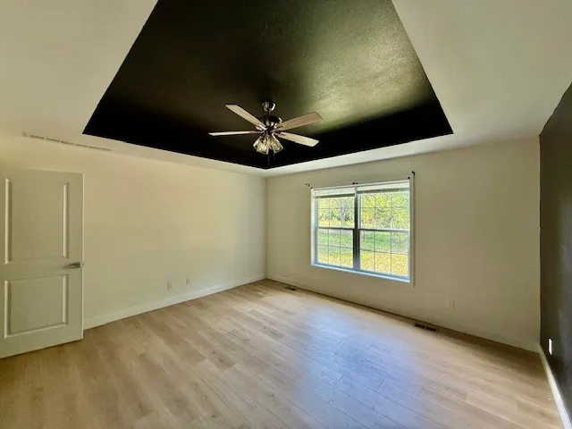 an empty room with wooden floor fan and windows