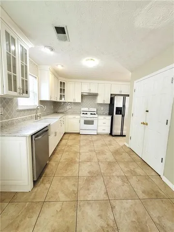 a large kitchen with a stove a sink dishwasher a refrigerator and white cabinets with wooden floor