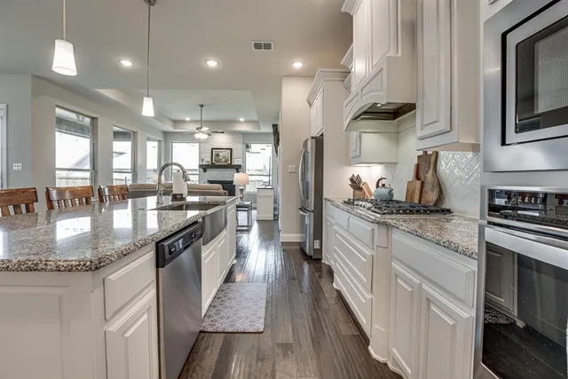 a kitchen with stainless steel appliances granite countertop a stove a refrigerator and a white cabinets with wooden floor