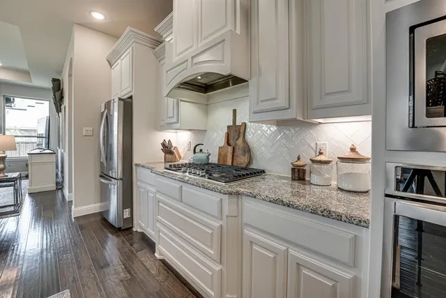 a kitchen with stainless steel appliances kitchen island granite countertop a stove a sink a refrigerator and white cabinets with wooden floor