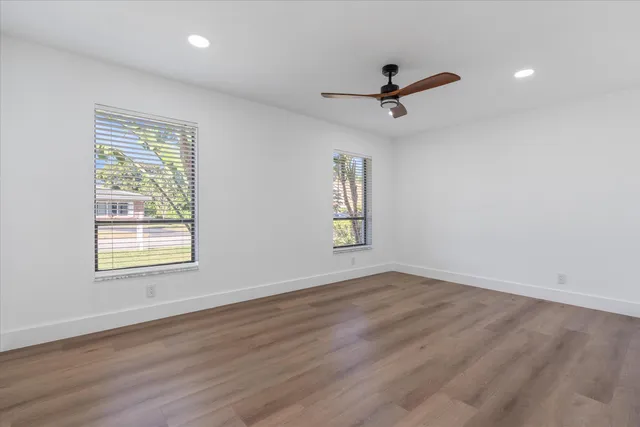 an empty room with wooden floor ceiling fan and windows