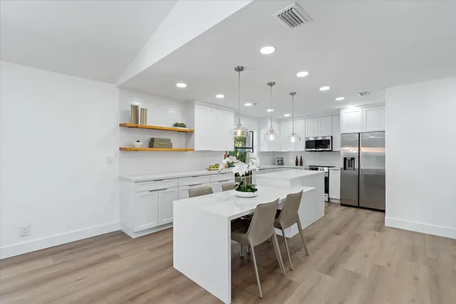 a kitchen with a dining table chairs wooden floor cabinets and stainless steel appliances