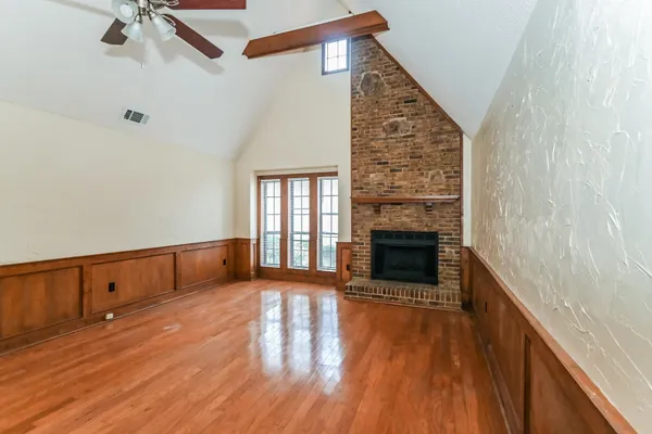 a view of an empty room with wooden floor fireplace and a window