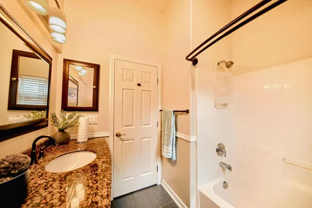 a bathroom with a granite countertop sink mirror vanity and a bathtub