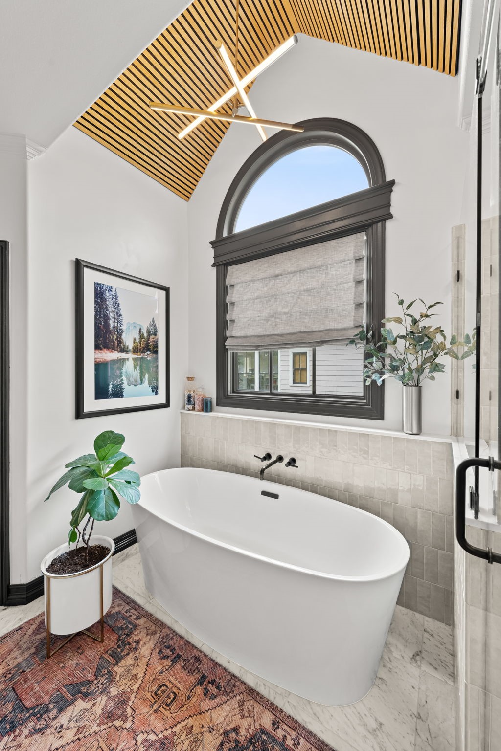 520 Oxford Street, Unit F Houston, TX 77007 - Photo 21 of 38 The freestanding soaking tub takes center stage beneath a dramatic arched window and vaulted ceiling with a warm wood slat inlay and geometric linear chandelier. Wall-mounted matte black tub filler hardware and large-format marble tile flooring bring a refined, hotel-like quality to this fully renovated primary bath.