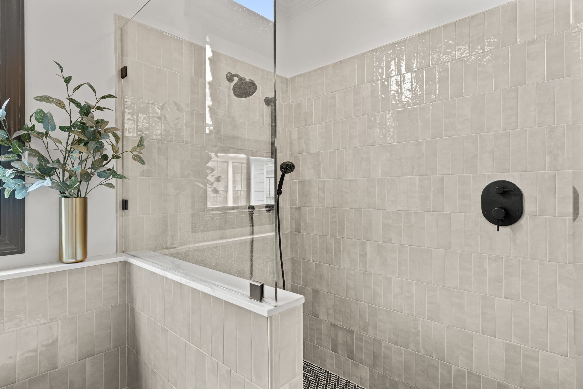 520 Oxford Street, Unit F Houston, TX 77007 - Photo 23 of 38 The walk-in shower is finished with floor-to-ceiling handmade ceramic tile in a soft warm gray, complemented by matte black hardware, a rain showerhead, and a handheld spray fixture. A glass panel wall and mosaic penny tile floor complete this meticulously designed shower enclosure.