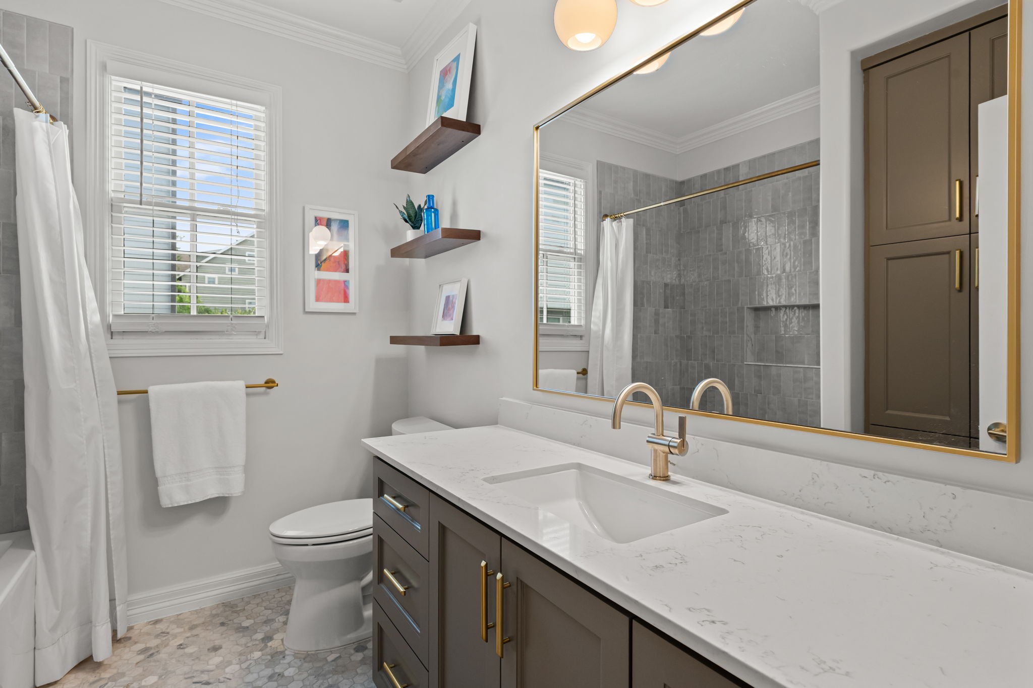520 Oxford Street, Unit F Houston, TX 77007 - Photo 28 of 38 The secondary bath received a full gut-and-rebuild renovation in 2025, now showcasing a quartz countertop vanity with gold hardware, a gold-framed mirror, globe vanity lighting, walnut floating shelves, hexagonal mosaic tile flooring, and a tiled tub/shower surround. Every finish reflects the same elevated design sensibility found throughout the home.