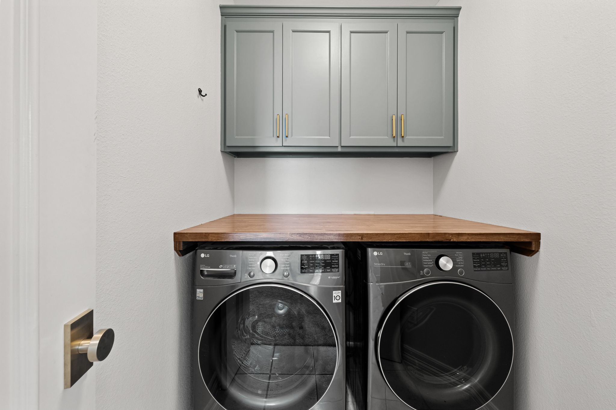 520 Oxford Street, Unit F Houston, TX 77007 - Photo 30 of 38 The upstairs utility room is outfitted with a full-size front-load washer and dryer set included with the home, a butcher block folding surface, and custom cabinetry with gold hardware overhead for additional storage. Keeping laundry conveniently located near all bedrooms adds meaningful everyday functionality.