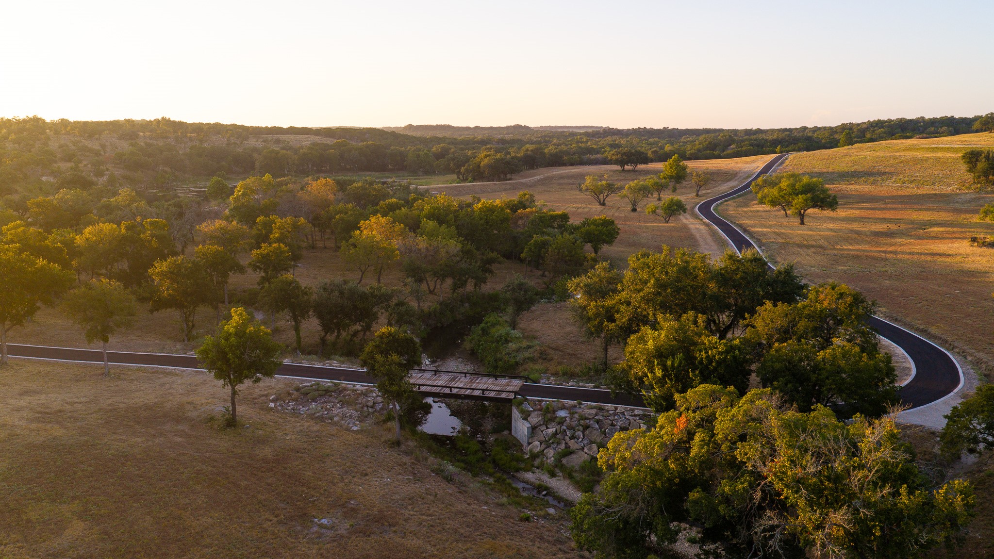 920 Ryan Road Bertram, TX 78605 - Photo 12 of 40 A paved path winds through rolling hills, mature trees, and a quiet creek crossing.