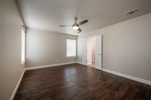 an empty room with wooden floor ceiling fan and windows