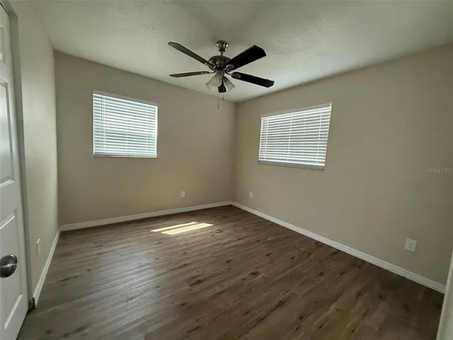 an empty room with wooden floor fan and windows