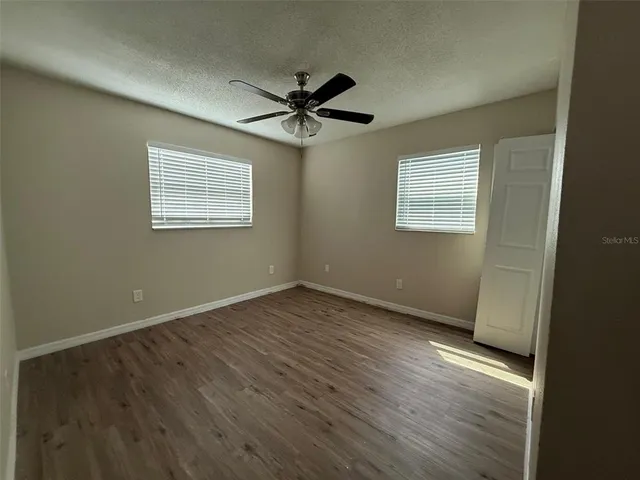 an empty room with wooden floor fan and windows