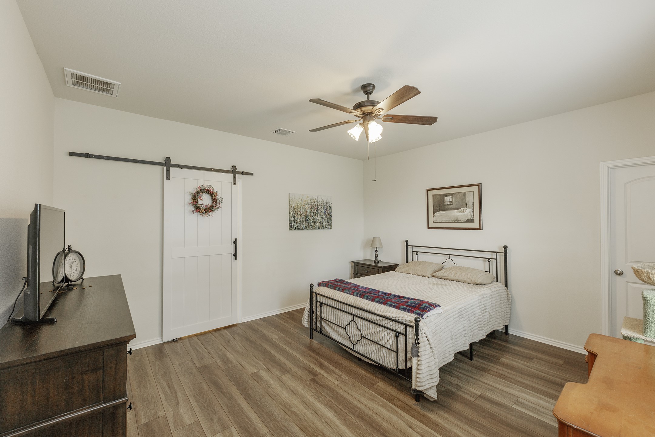 125 Janice Road Taylor, TX 76574 - Photo 15 of 26 Bedroom featuring wood-finish flooring, a white barn door, and a ceiling fan with integrated lighting