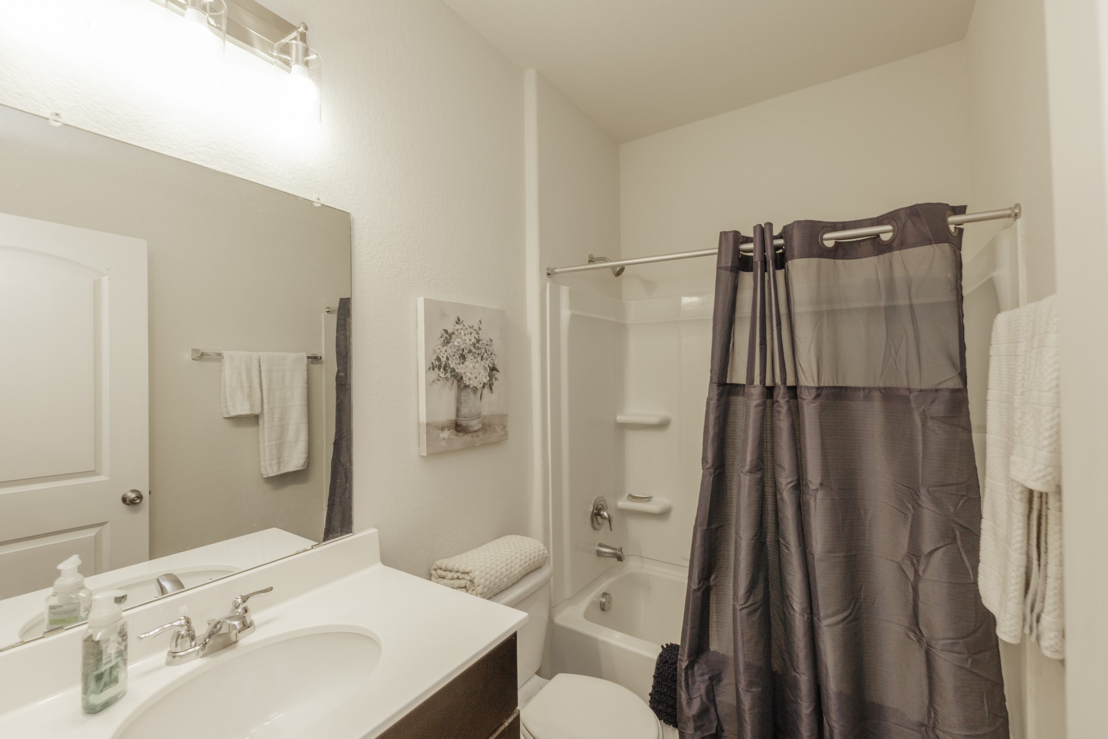 125 Janice Road Taylor, TX 76574 - Photo 20 of 26 Bathroom featuring a white bathtub with an integrated shower, a vanity with a white countertop and undermount sink, a large mirror, and a wall-mounted light fixture