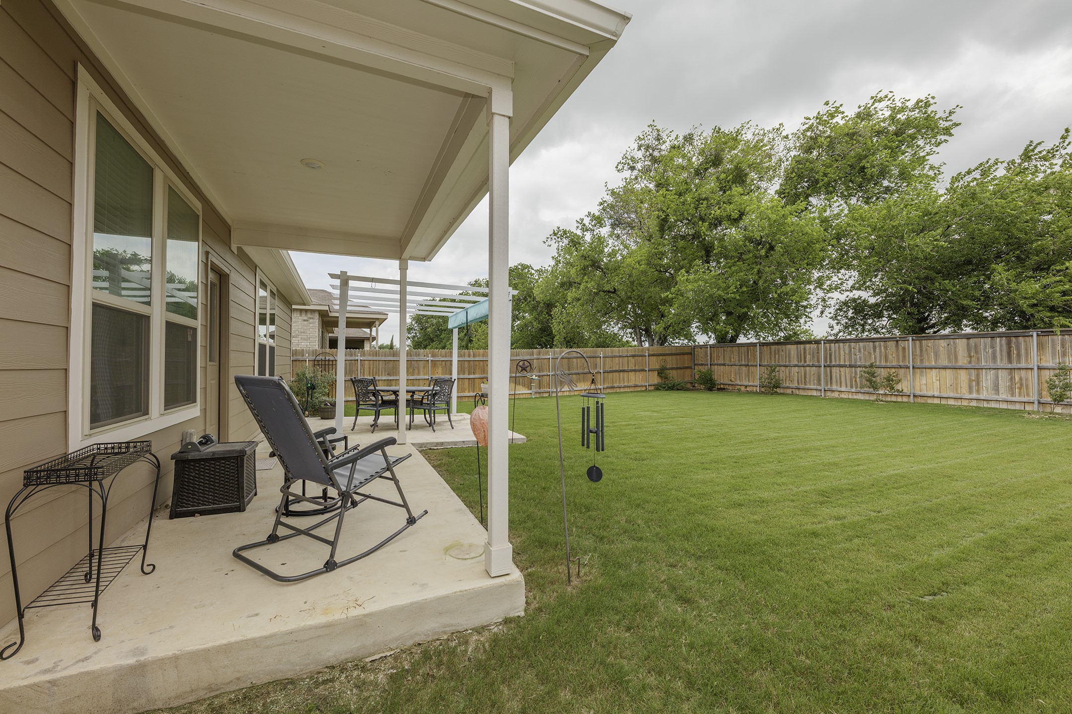 125 Janice Road Taylor, TX 76574 - Photo 22 of 26 Expansive backyard featuring a covered concrete patio, a secondary open concrete patio with a white pergola, a full wood privacy fence, and mature trees beyond the fence line
