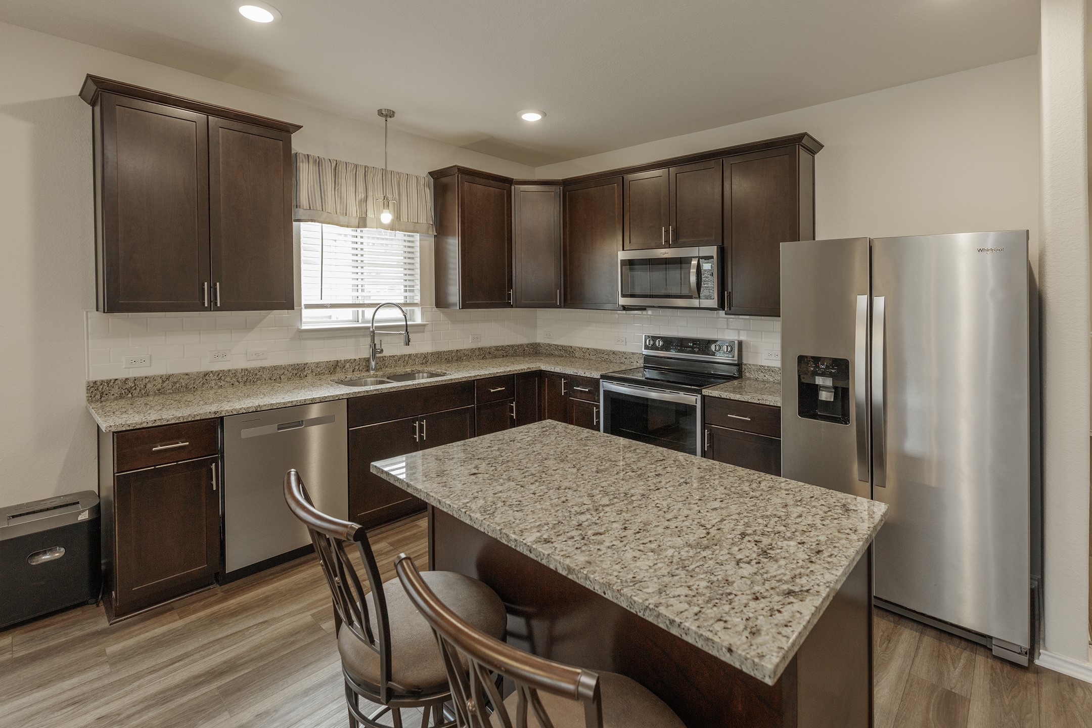 125 Janice Road Taylor, TX 76574 - Photo 6 of 26 Kitchen featuring dark wood cabinetry, granite countertops, wood-finish flooring, stainless steel appliances, and a central island with bar seating