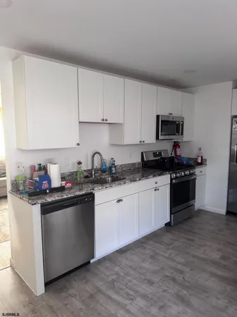 a kitchen with stainless steel appliances granite countertop a stove top oven a sink a refrigerator and white cabinets