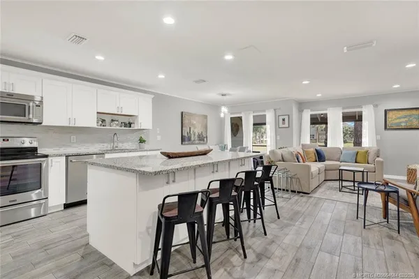 a large white kitchen with stainless steel appliances granite countertop a stove a sink a dining table and chairs
